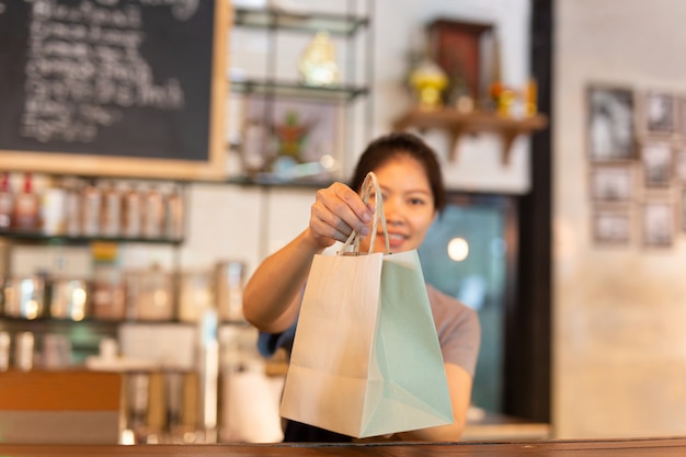 Camarera en el mostrador dando bolsa de papel ecológica con bebida para llevar en la cafetería