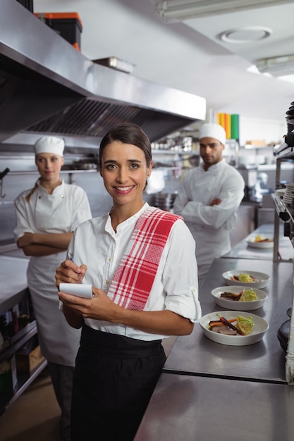 Camarera de pie con personal de cocina en cocina comercial