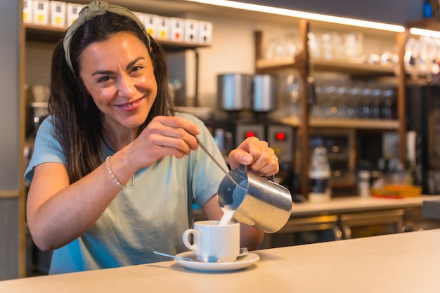 Camarera sonriente en la cafetería preparando café y agregando la leche se levantan las restricciones de covid y se elimina el uso obligatorio de máscaras