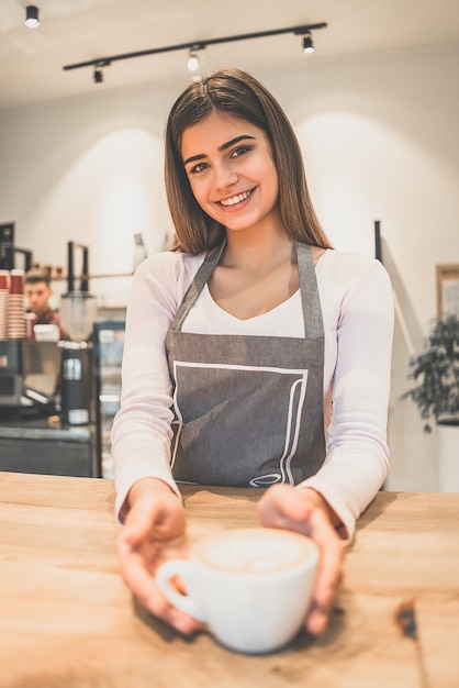 La camarera de la sonrisa sosteniendo una taza de café en un café