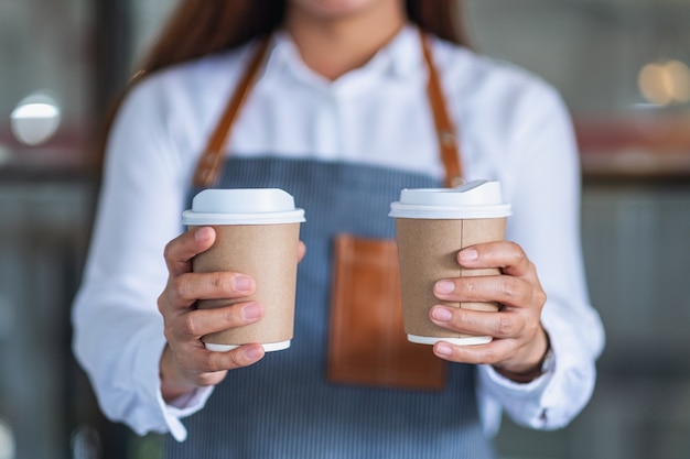 Una camarera sosteniendo y sirviendo dos vasos de papel de café caliente en el café