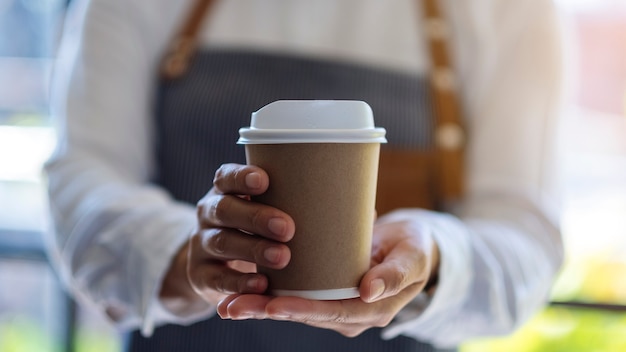 Una camarera sosteniendo y sirviendo una taza de café caliente en el café de papel