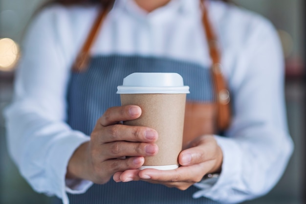 Una camarera sosteniendo y sirviendo una taza de café caliente en el café de papel