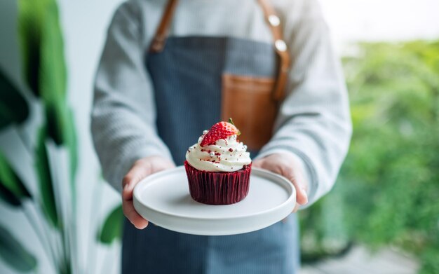 Una camarera sosteniendo y sirviendo un trozo de cupcake de terciopelo rojo.