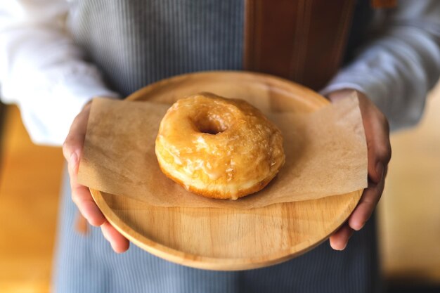 Una camarera sosteniendo y sirviendo un trozo de rosquilla casera en bandeja de madera