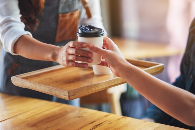 Una camarera sosteniendo y sirviendo vasos de papel de café caliente al cliente en la cafetería