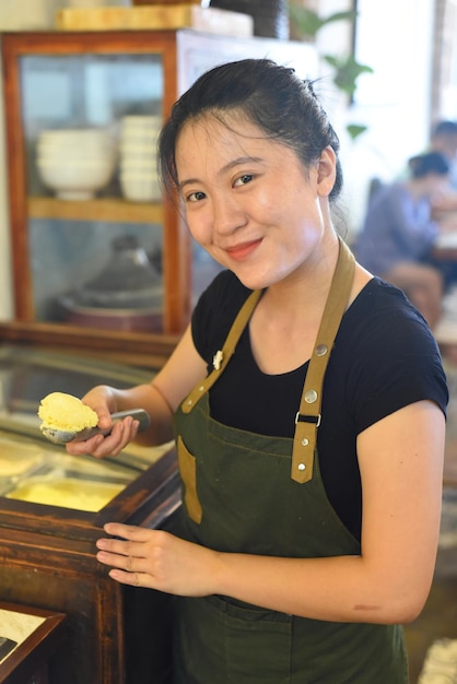 Camarera vietnamita mostrando una bola de helado de mango casero en el café