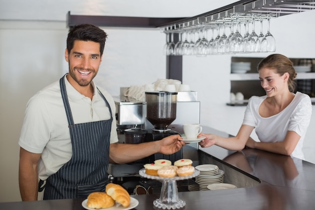 Camarero amigable dando café a una mujer en la cafetería