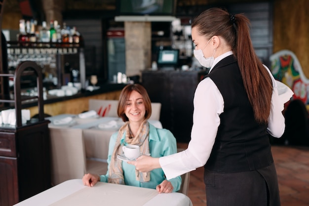 Un camarero de aspecto europeo con una máscara médica sirve café.