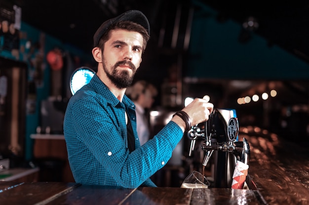 Camarero barbudo vertiendo bebida alcohólica fresca en los vasos en el bar