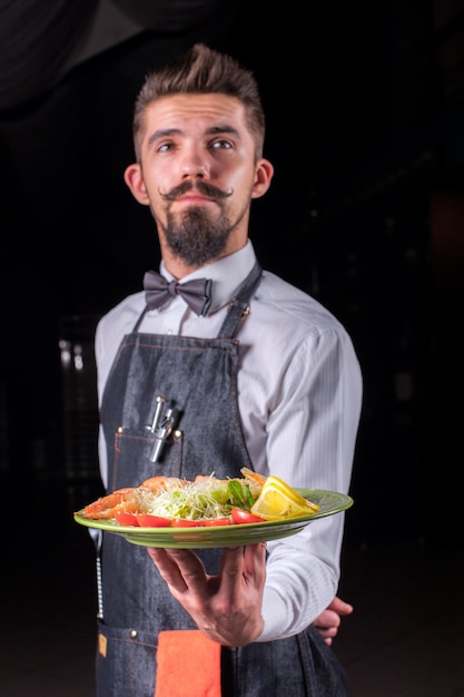 El camarero con bigotes sirve un plato con un plato preparado en un evento festivo.