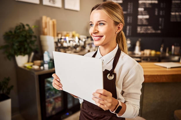 Camarero de café feliz en delantales con papel blanco en la mano