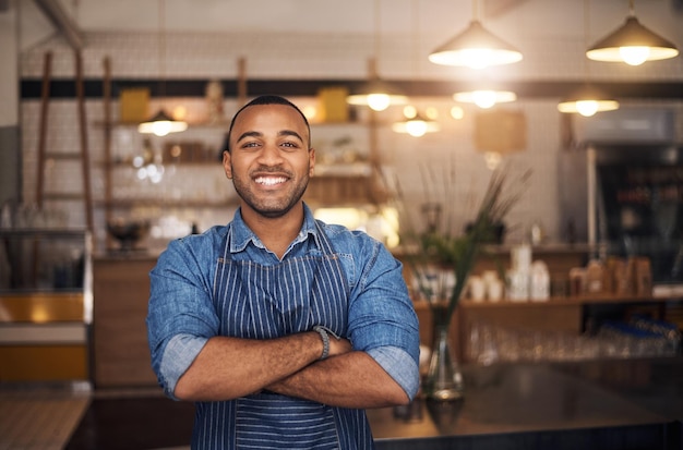 Camarero de cafetería y retrato de hombre africano en restaurante para trabajo de servicio y brazos cruzados en café Inicio de bistró de propietario de pequeña empresa y sonrisa de barista masculino en cafetería lista para servir