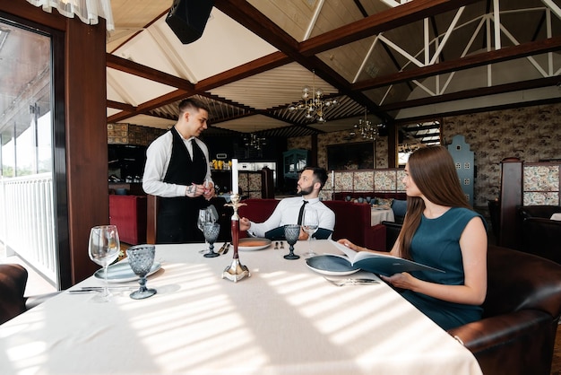 Un camarero elegante atiende a una pareja joven de un hombre y una mujer que acudieron a una cita a un restaurante gourmet Atención al cliente en el restaurante y establecimientos de catering