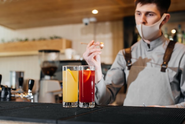 Un camarero elegante con máscara y uniforme durante una pandemia está preparando cócteles en una fiesta El trabajo de los restaurantes y cafeterías durante la pandemia