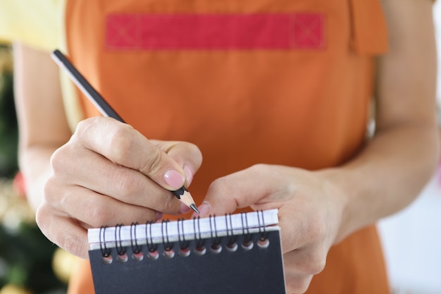 Camarero escribiendo platos ordenados en un cuaderno con un lápiz de cerca. Concepto de menú de vacaciones