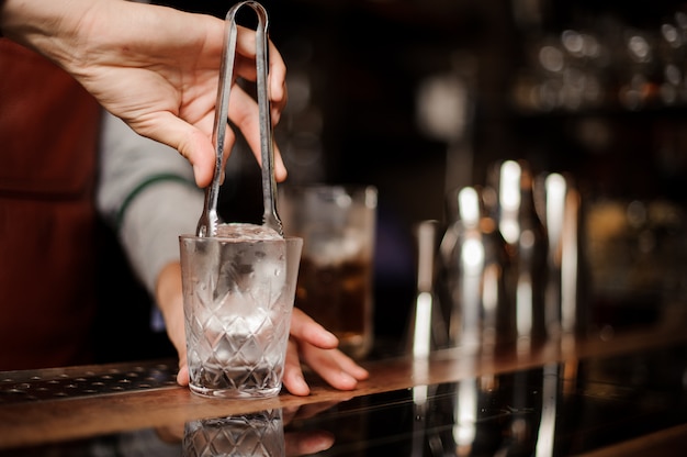 Camarero está poniendo un hielo en un vaso de chupito