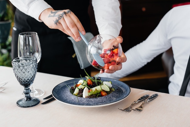 El camarero hace una exquisita ración de ensalada de mariscos, atún y caviar negro en una hermosa porción en la mesa del restaurante. Exquisitos manjares de la alta cocina en primer plano.