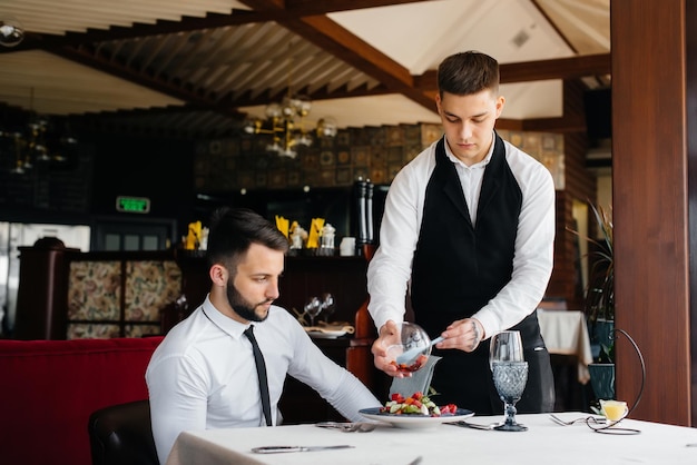 El camarero hace una exquisita ración de ensalada de mariscos, atún y caviar negro en una hermosa porción en la mesa del restaurante. Exquisitos manjares de la alta cocina en primer plano.