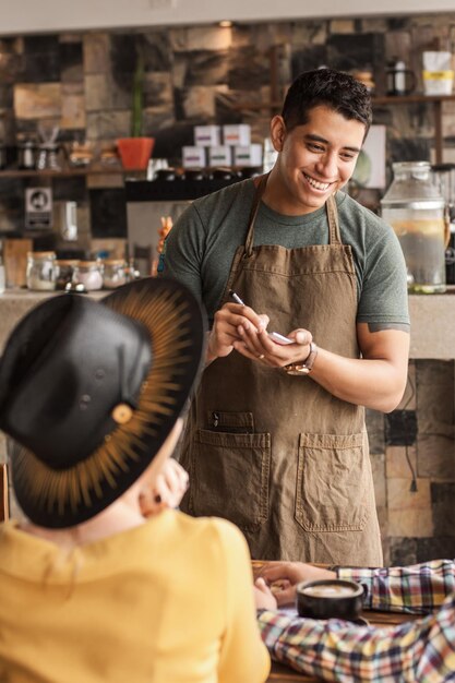 Camarero latino feliz que toma una orden en una cafetería