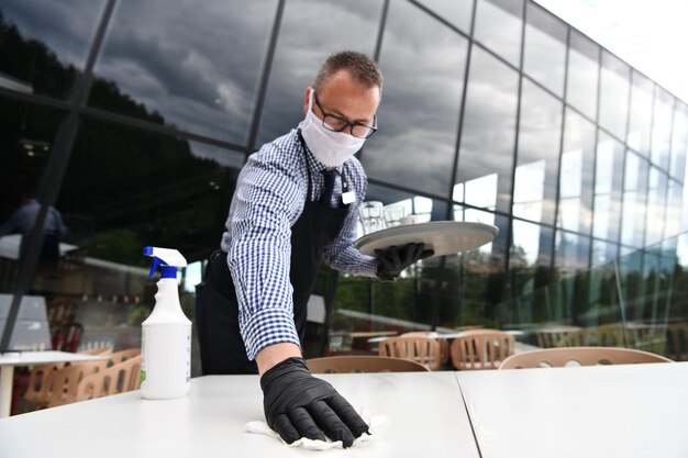 Foto camarero limpiando la mesa con spray desinfectante en un restaurante con máscara médica protectora y guantes nuevo concepto normal