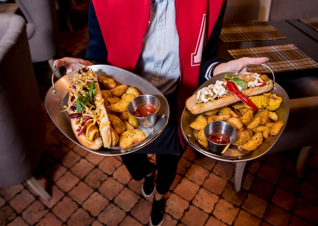 Camarero, llevando dos platos con un gran hot dogs y papas fritas.