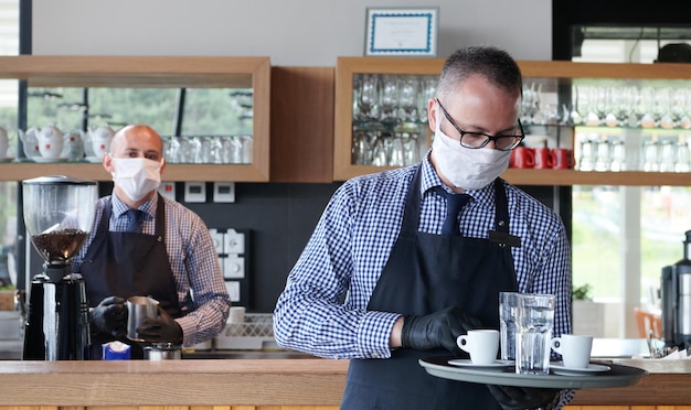 el camarero con una máscara de protección médica sirve el café en el restaurante durante la pandemia del coronavirus que representa un nuevo concepto normal