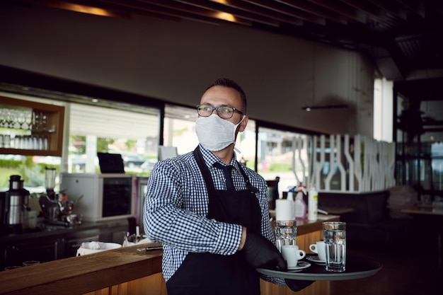 el camarero con una máscara de protección médica sirve el café en el restaurante durante la pandemia del coronavirus que representa un nuevo concepto normal