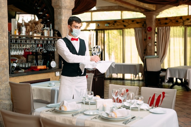 Un camarero con una máscara protectora médica sirve la mesa en el restaurante.