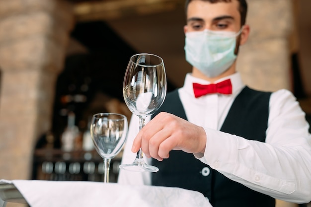 Un camarero con una máscara protectora médica sirve la mesa en el restaurante.