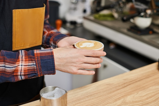 Camarero masculino en delantal sosteniendo una taza de bebida caliente