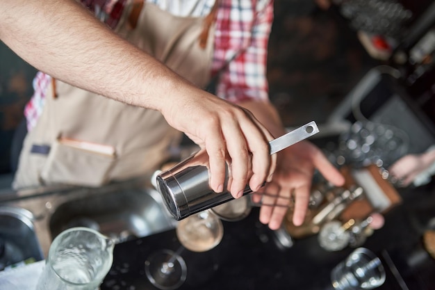 Foto el camarero masculino profesional vierte un cóctel de una coctelera