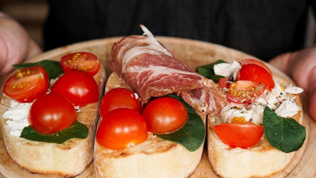 Camarero mujer sosteniendo una bandeja de madera con bruschetta con tomates cherry en la mano. Delicioso aperitivo italiano
