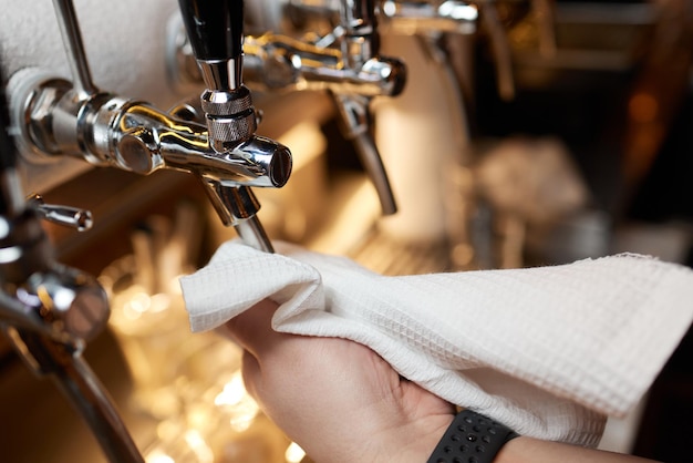 Camarero o cantinero limpiando grifos de cerveza en el mostrador de pub y restaurante