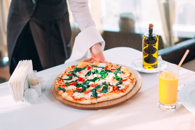 El camarero pone pizza sobre la mesa en el restaurante.