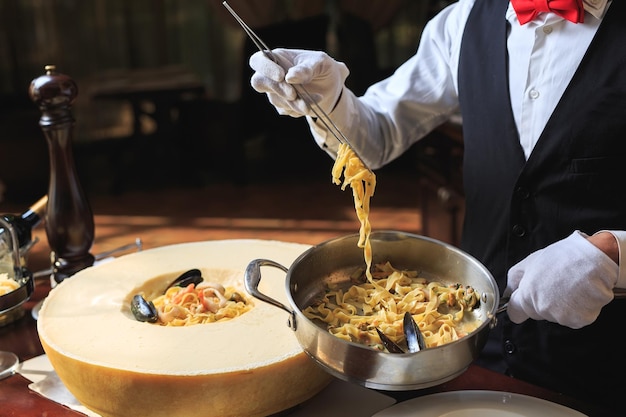 El camarero prepara Pasta con marisco y queso parmesano