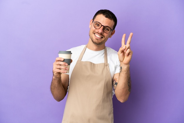 Camarero de restaurante brasileño sobre fondo púrpura aislado sonriendo y mostrando el signo de la victoria