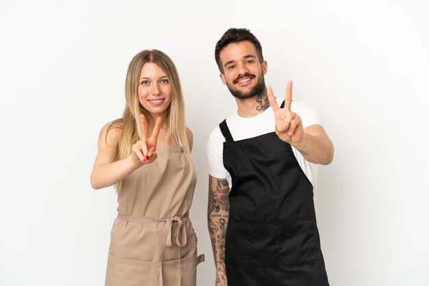 Camarero de restaurante sobre fondo blanco aislado sonriendo y mostrando el signo de la victoria