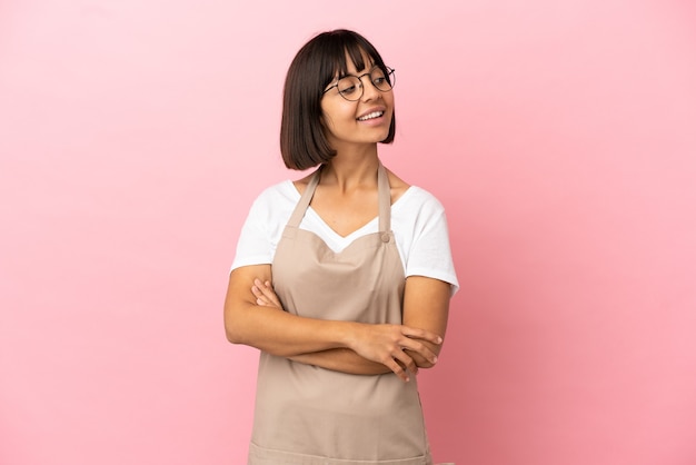 Camarero de restaurante sobre fondo rosa aislado con los brazos cruzados y feliz