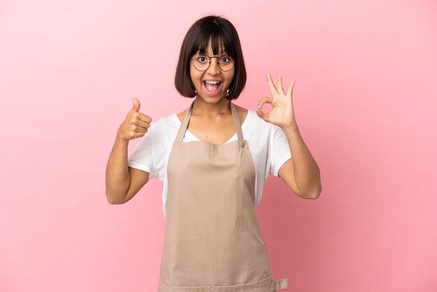 Camarero de restaurante sobre fondo rosa aislado que muestra el signo de ok y el pulgar hacia arriba gesto