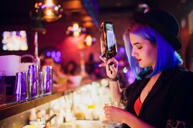 Foto camarero de sexo femenino que hace el cóctel usando la coctelera en pub.