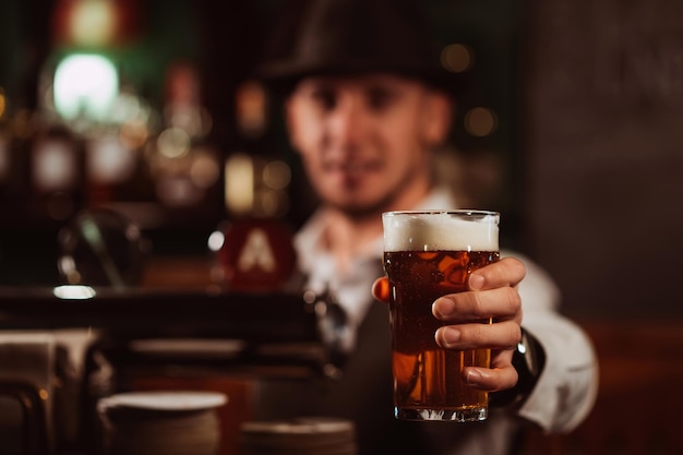 El camarero sirve en la mano un vaso de cerveza ligera con espuma en el mostrador del bar