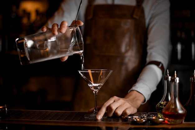 Camarero sirviendo una bebida alcohólica de la taza de medir al vaso de martini