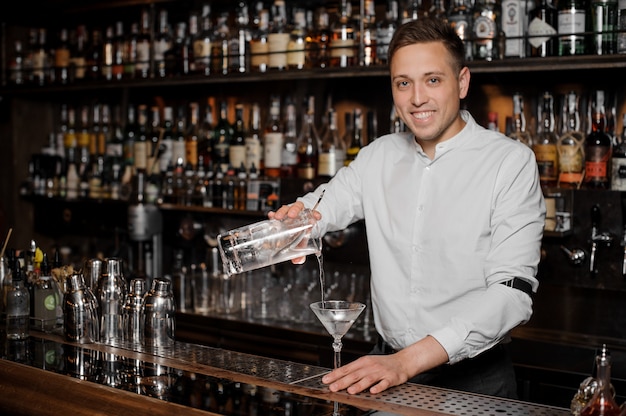 Camarero sonriente agregando una bebida alcohólica en el vaso de martini