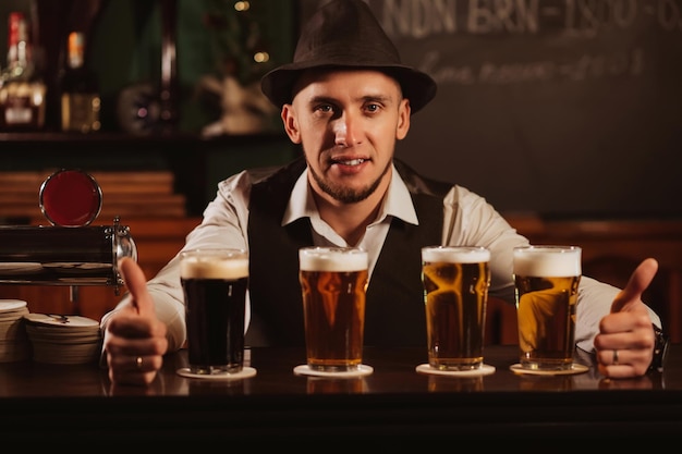 Camarero sonriente feliz en el mostrador del bar con cuatro vasos de cerveza de barril