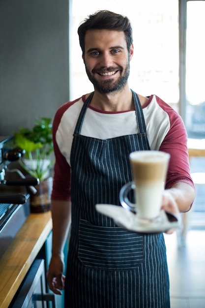 Camarero sonriente sosteniendo una taza de café frío en el mostrador de la cafetería