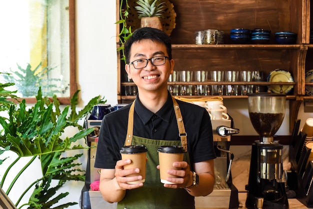 Camarero sonriente vietnamita sosteniendo vasos de papel con café en un café