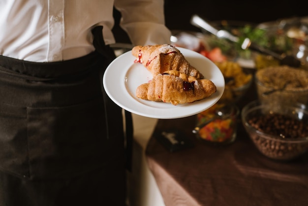 Un camarero sosteniendo un plato con croissants en el restaurante.