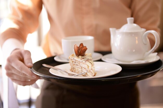 Foto el camarero sostiene la bandeja con tazas de té y pastel cerca