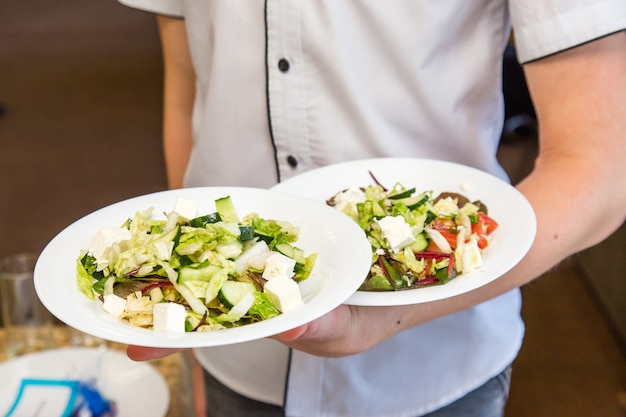 Camarero sujetar dos platos de ensalada, trabajar en evento.